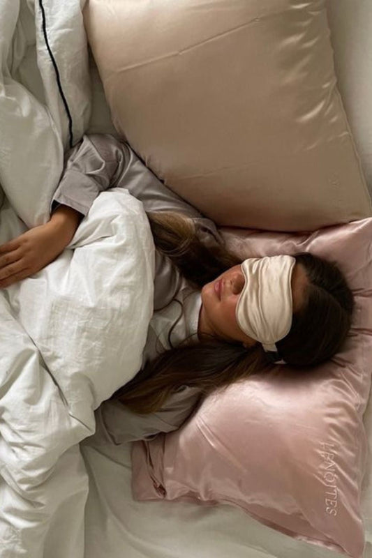 Femme dormant sur une taie d’oreiller en satin avec un masque en satin sur les yeux sous une couverture 